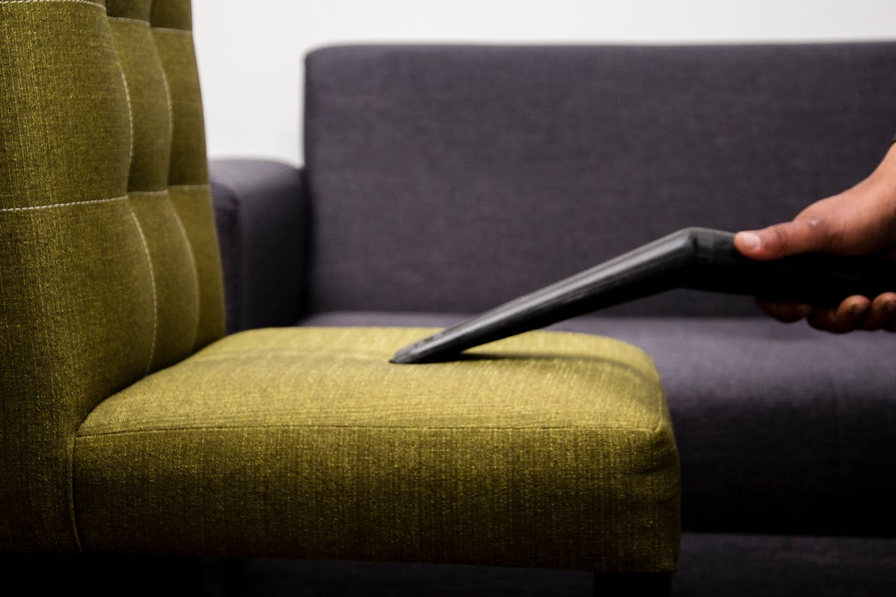 our-story Close-up of a person vacuuming a modern sofa chair indoors, highlighting cleaning service.